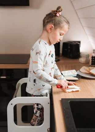 Meisje smeert brood aan het aanrecht in de STEP'n'SIT® 2-in-1 keukentoren wit met steunpoten