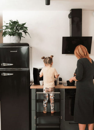 Kind helpt bij koffiezetten aan het aanrecht in de STEP'n'SIT® 2-in-1 keukentoren zwart met steunpoten