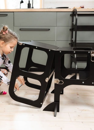 Meisje klapt de STEP'n'SIT® 2-in-1 keukentoren zwart met steunpoten om van toren naar tafel met zitje