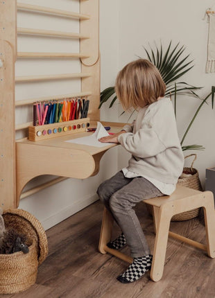 Kind zit op houten stoel en schrijft aan tafel bevestigd aan Zweedse klimwand