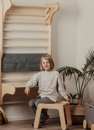 Kind zit op houten stoel voor tafel bevestigd aan Zweedse klimwand tegen witte muur
