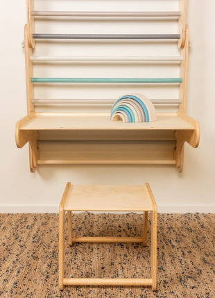 Houten tafel bevestigd aan Zweedse klimwand met pastel regenboogstapelaar erop
