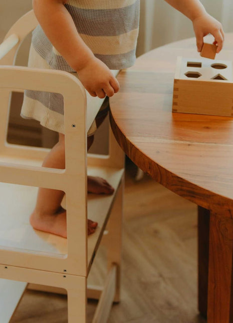 Kind staat op naturel Leg&Go transformeerbare keukentoren 2-in-1 en speelt met houten vormen aan tafel