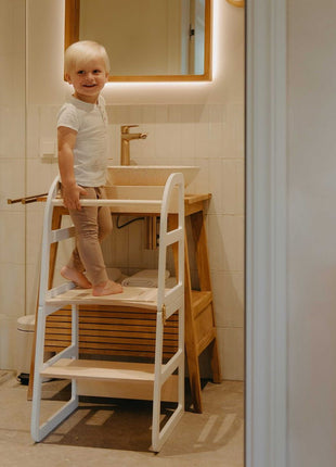 Lachend kind staat veilig op witte Leg&Go transformeerbare keukentoren 2-in-1 bij badkamerwastafel.