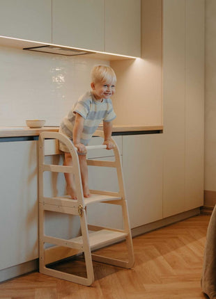Kind leunt op veiligheidsbeugel van witte Leg&Go transformeerbare keukentoren 2-in-1 bij keukenblad.