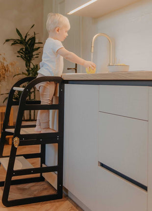 Kind staat op zwarte Leg&Go transformeerbare keukentoren 2-in-1 en werkt aan keukenblad.