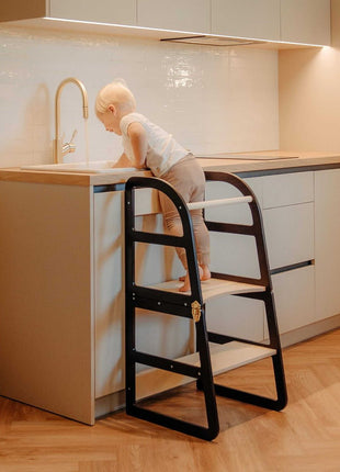 Kind staat op zwarte Leg&Go transformeerbare keukentoren 2-in-1 en wast handen bij keukenkraan.