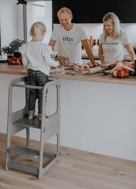 Kind staat op grijze Transformeerbare Keukentoren bij aanrecht met gesneden groenten.