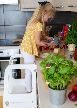 Kind gebruikt witte Transformeerbare Keukentoren tijdens wegzetten van blauwe kom op keukenblad.