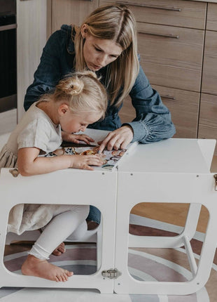 Kind leest met volwassene aan witte Transformeerbare Keukentoren in tafelstand.