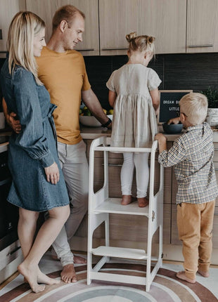 Kind staat op witte Transformeerbare Keukentoren aan aanrecht met gezin.