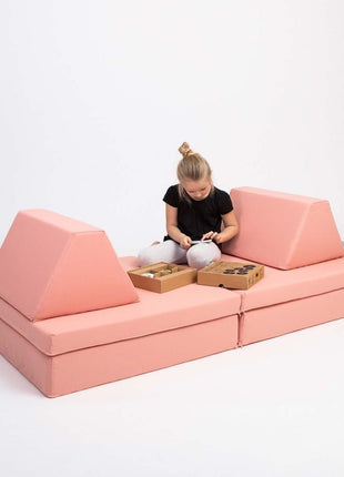 Kind speelt aan tafelvormige opstelling van de Monboxy Montessori speelbank in zalmroze – bevordert sociaal spel en interactie.