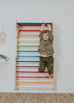 Kind hangt aan bovenste sport van Zweeds klimwand systeem regenboog tegen witte muur